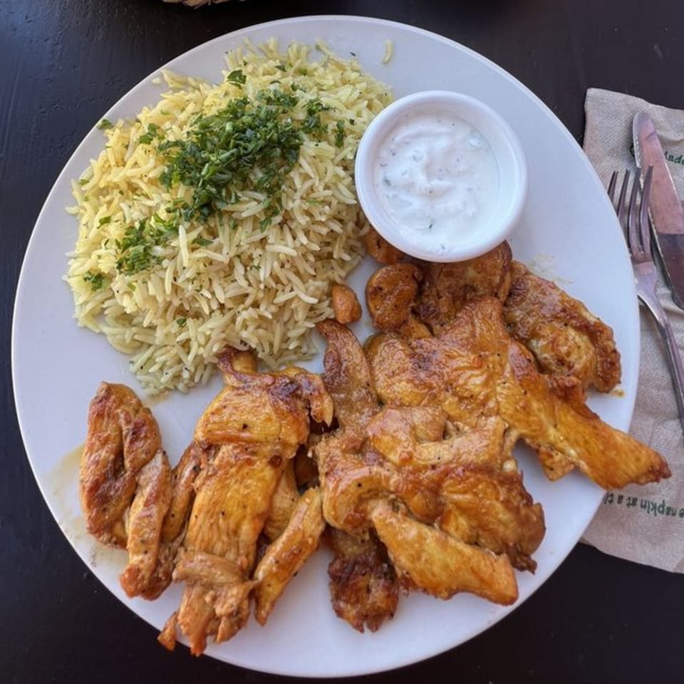 Mediterranean chicken shawarma with rice pilaf and a side of white sauce on a plate.