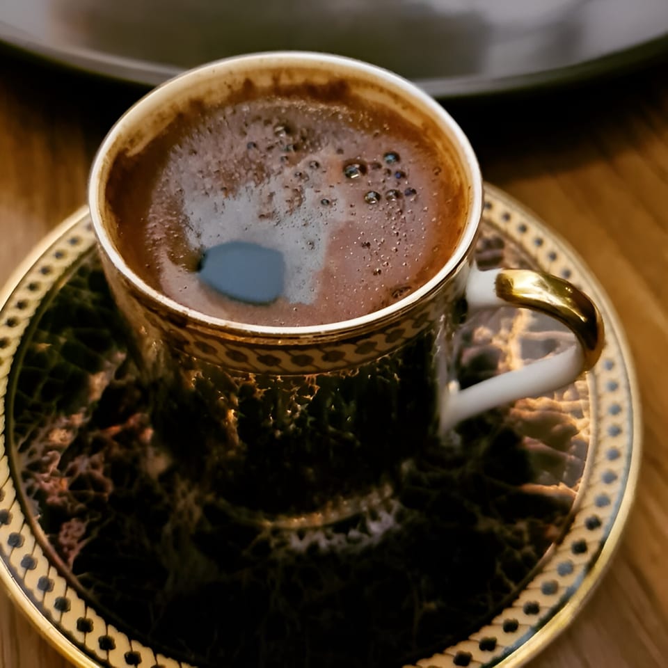 A cup of Turkish coffee with foam on top, in a decorative gold and black cup and saucer.